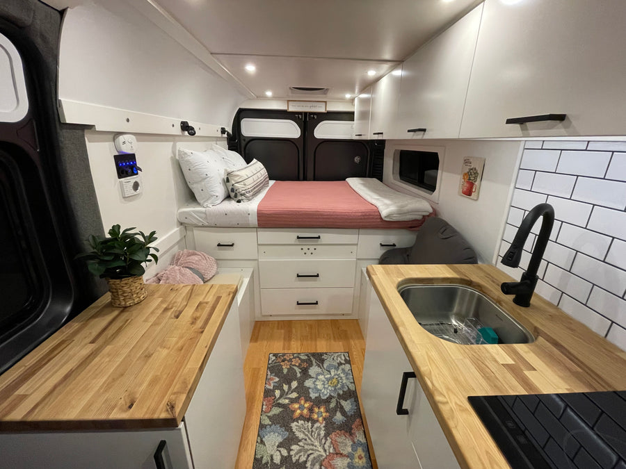 Cozy RV rental interior featuring a bed, butcher block countertops with sink/stovetop, and white storage cabinets.