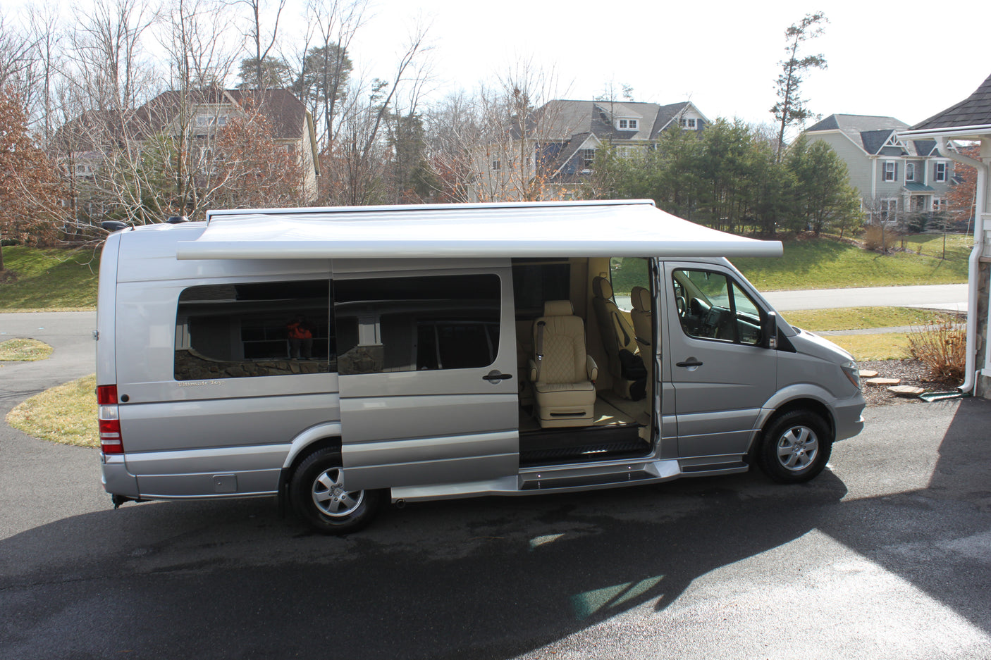 Silver Mercedes Sprinter luxury RV, ideal for rv rental adventures. Awning extended, side door open showing plush interior.