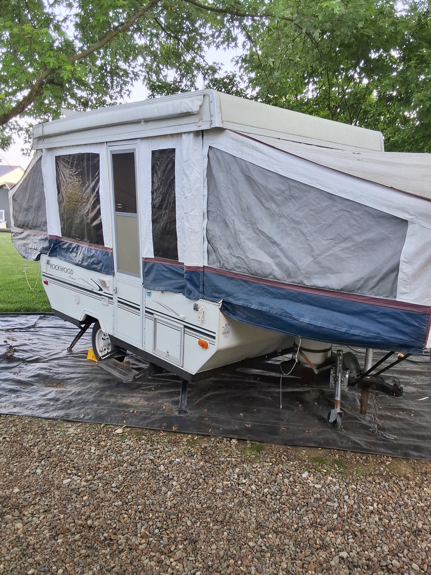 White Rockwood pop-up camper set up on gravel under trees. Ideal for an RV rental adventure.