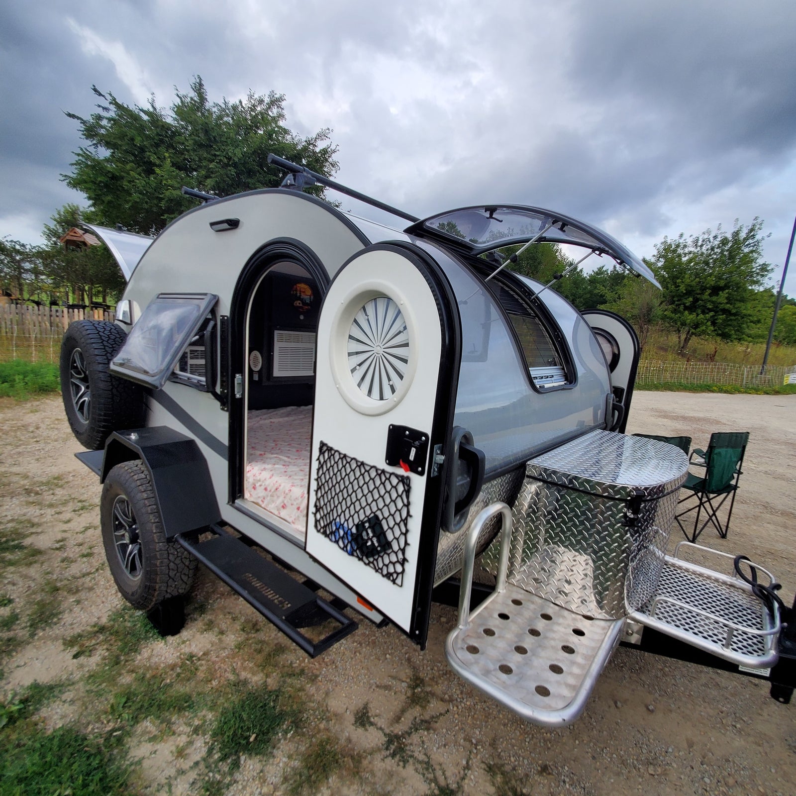 Compact teardrop RV rental, perfect for adventure. Open door reveals a cozy bed, AC unit, and front storage box.