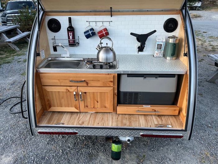 is parked at a campsite with its rear galley open.|Explore the outdoors with this teardrop RV rental