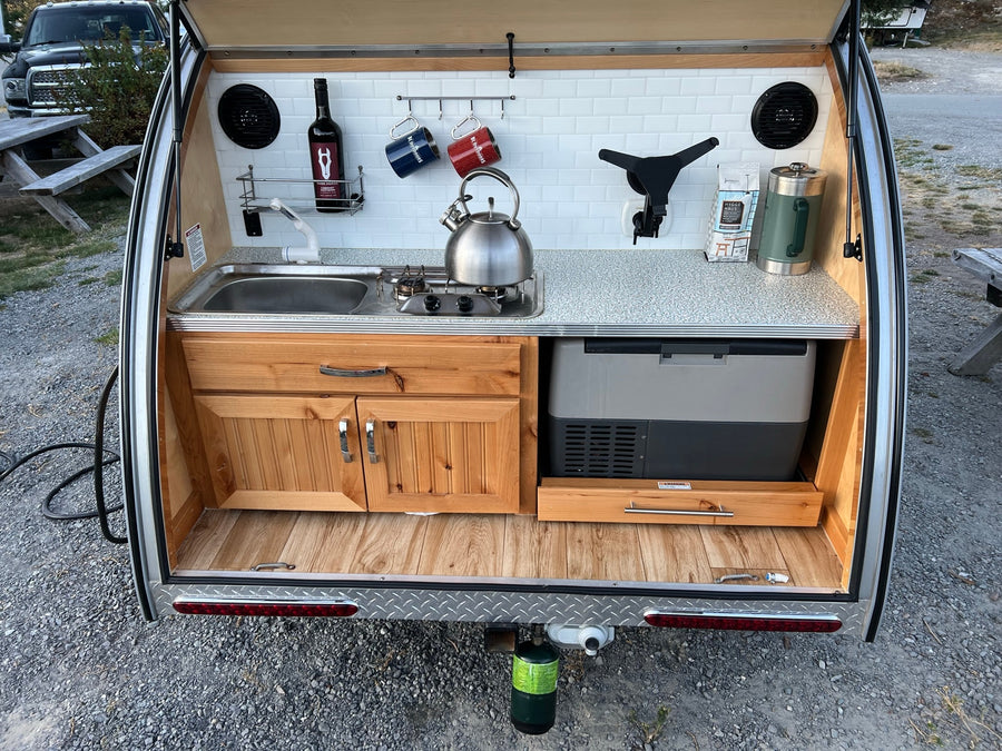 is parked at a campsite with its rear galley open.|Explore the outdoors with this teardrop RV rental