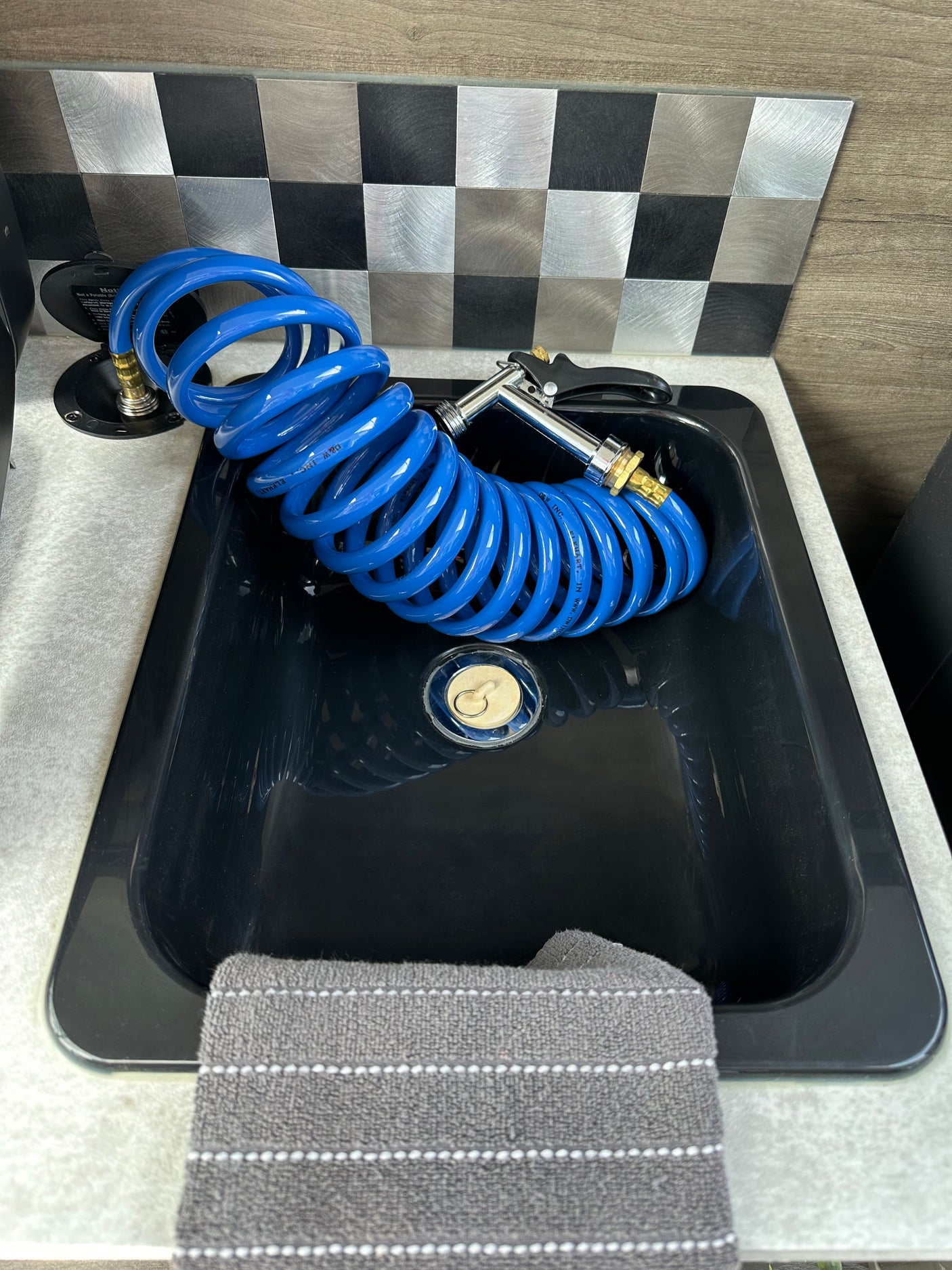 RV rental: A black utility sink with a blue coiled hose and spray nozzle. Non-potable water connection visible beside it, with a checkered backsplash.