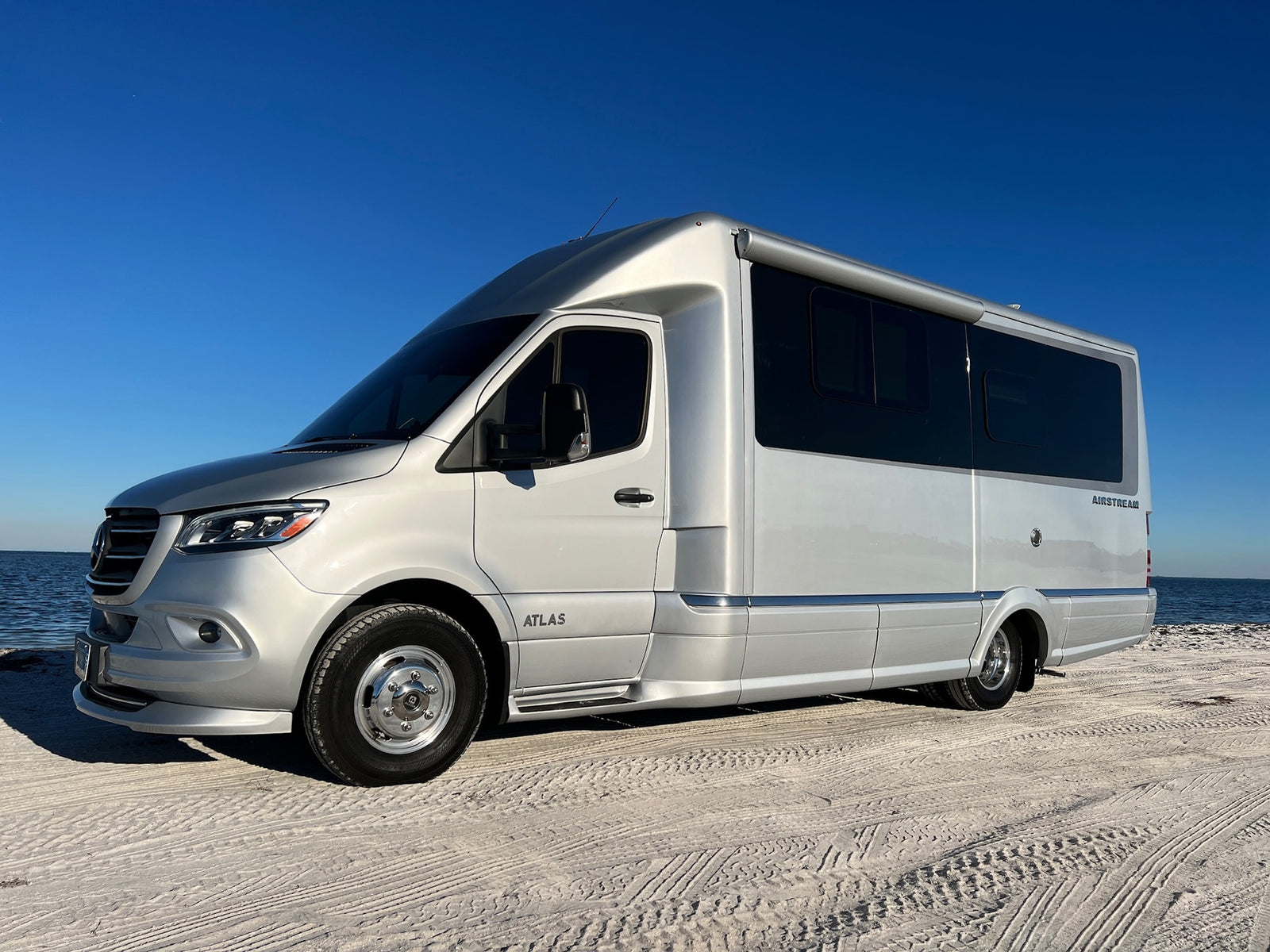 This silver Airstream Atlas, a Mercedes-Benz Sprinter RV rental, awaits adventure on a sandy beach.