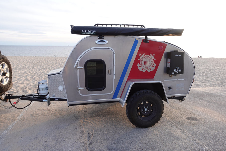 Unique USCG-themed overland trailer, available for RV rental, parked on a beach with ALLATOP gear & GASLAND heater.
