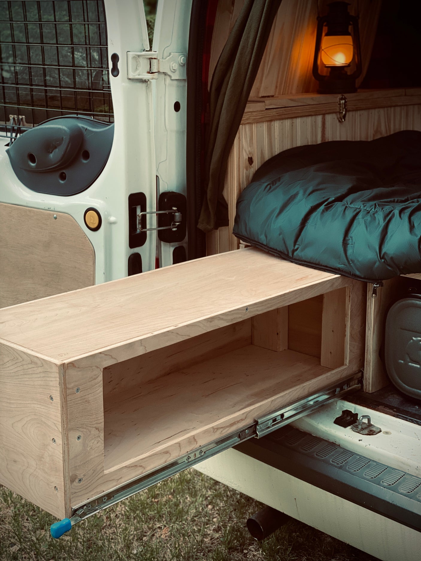 Cozy rv rental interior with a custom pull-out wooden drawer for storage and a compact sleeping area, lit by a warm lantern.