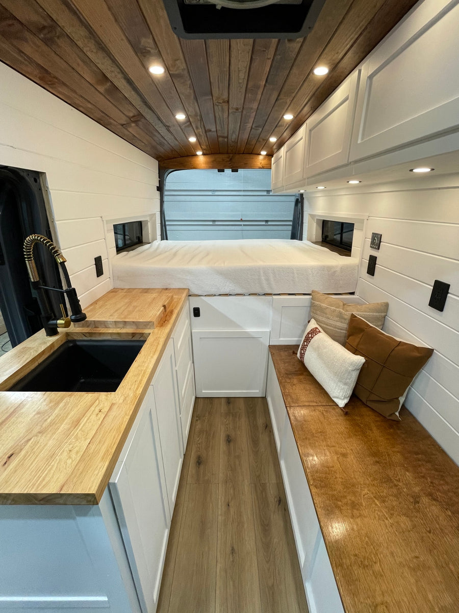 Step inside this RV rental! Cozy camper van interior featuring a kitchen, bed, and bench seating with wood details.