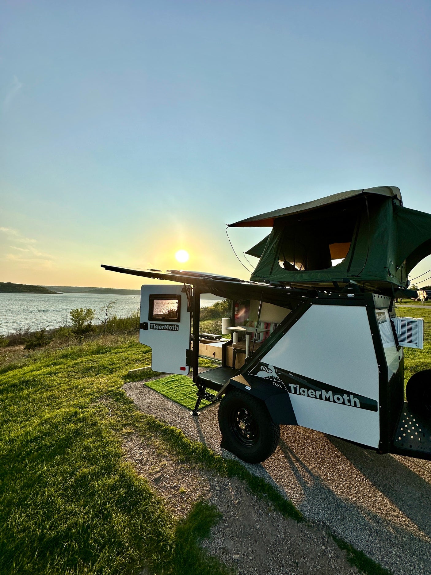 Experience outdoor adventure: This TigerMoth camper RV rental, with its rooftop tent & open kitchen, sits lakeside at sunset.