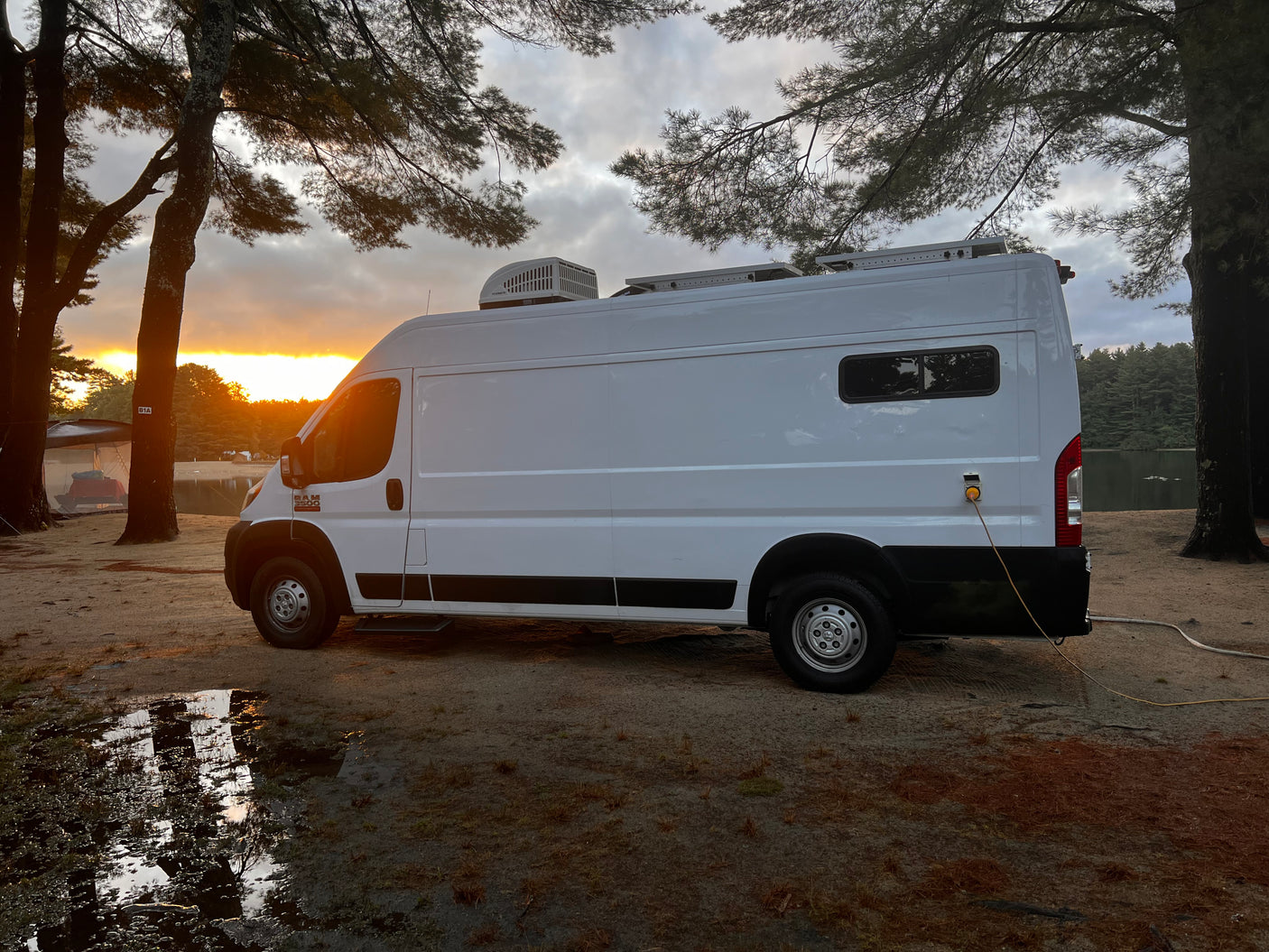 White RV rental van parked by a lake at stunning sunset. Ideal for a nature camping adventure, complete with power hookup.