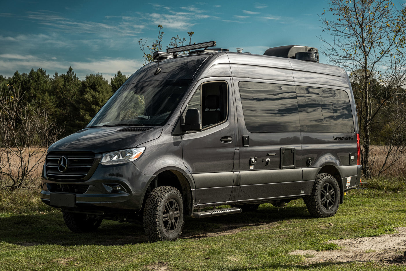 Dark grey Mercedes-Benz Sprinter camper van, an ideal rv rental, parked on grass. Off-road ready.