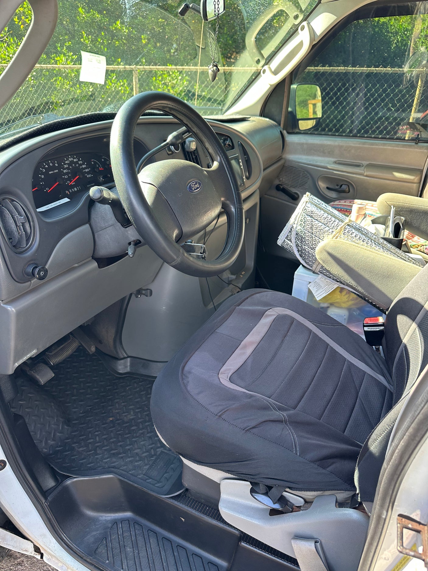 Interior of an RV rental van: Driver's view with Ford steering wheel, dashboard, seat cover, and sunshade. Ready for adventure.