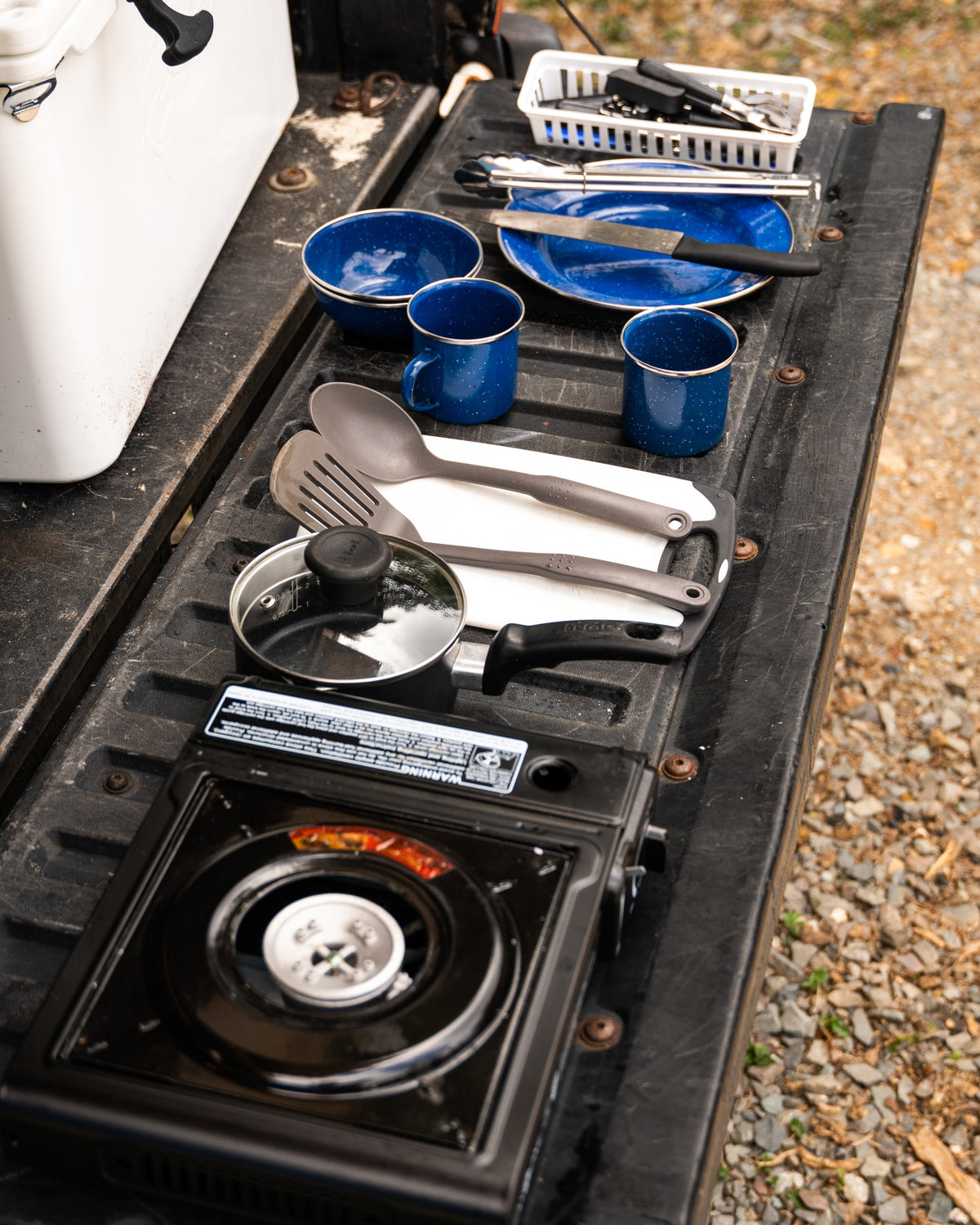 Essential RV rental gear: Blue speckled camping dishes, utensils, portable stove, and pot laid out for outdoor cooking.