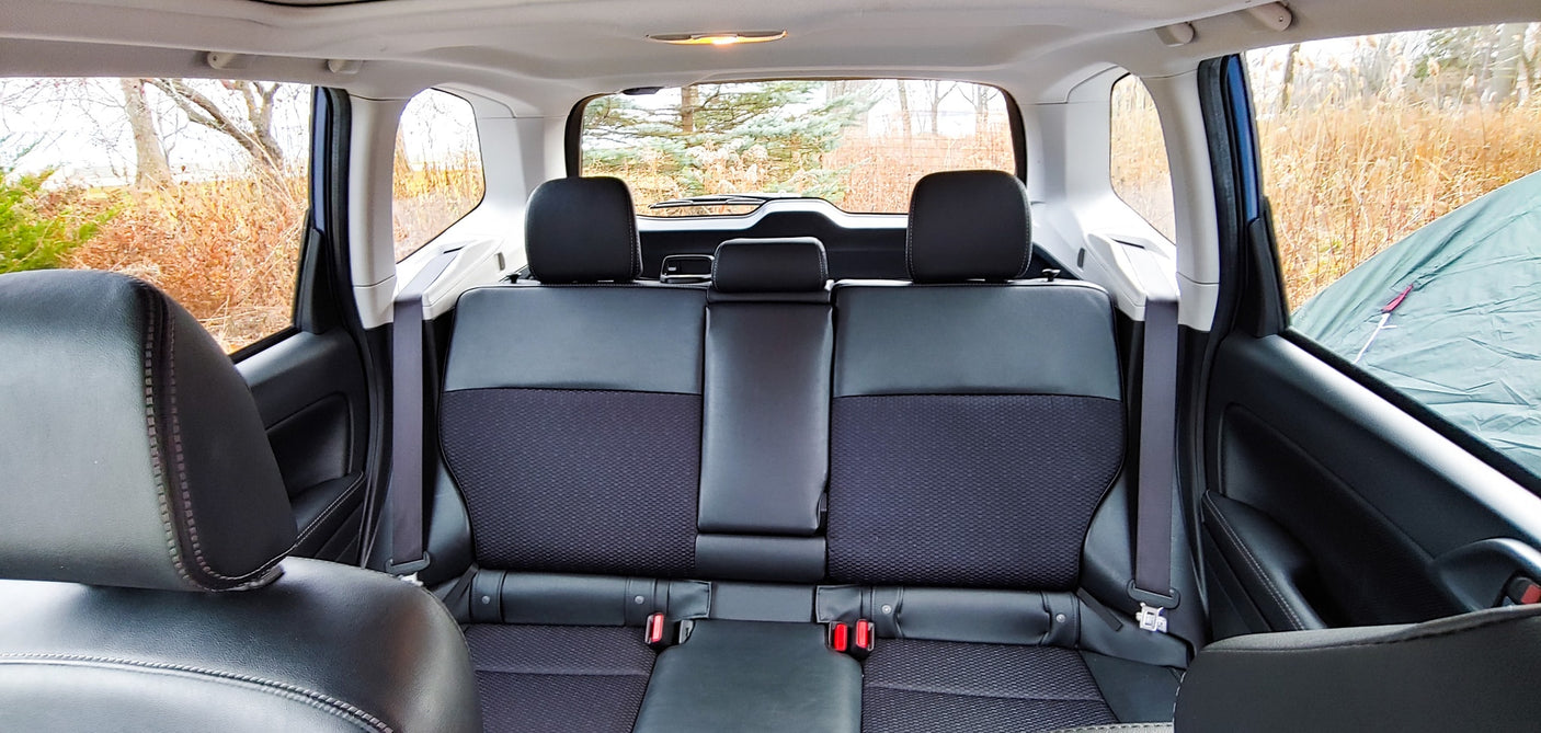 Inside a car: black rear seats and a view of trees/tent. Ready for camping trips, a compact alternative to an RV rental.