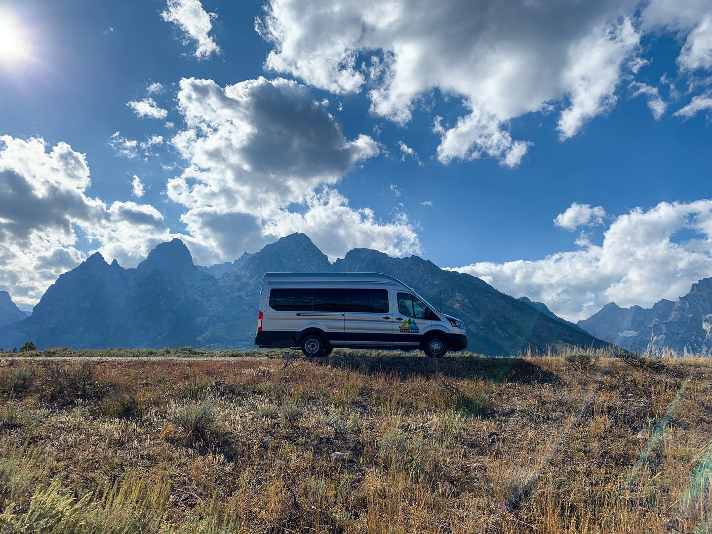 Silver WanderVans RV rental camper van overlooking majestic mountains under a bright, cloudy sky. Perfect for outdoor travel.