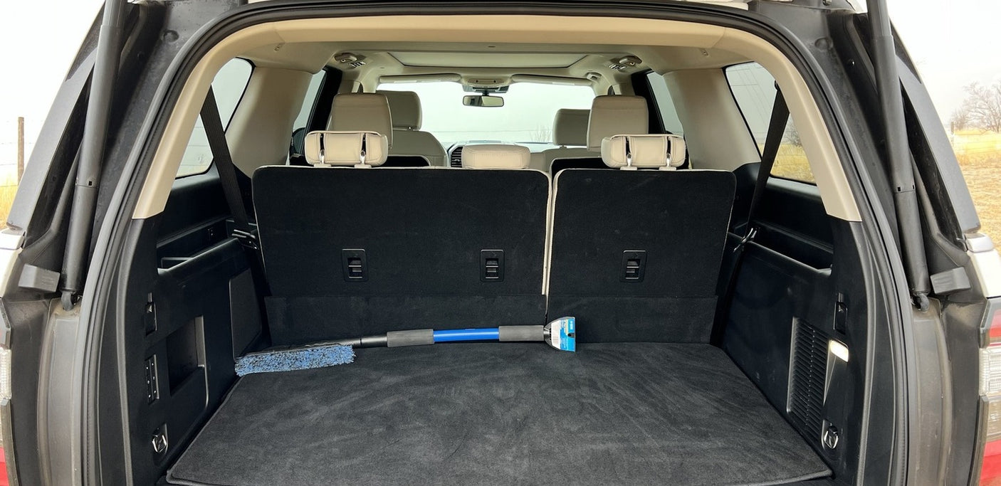 Inside a large SUV's trunk: folded third-row seats reveal vast cargo space. A cleaning tool rests. Ideal for RV rental trips or adventure.