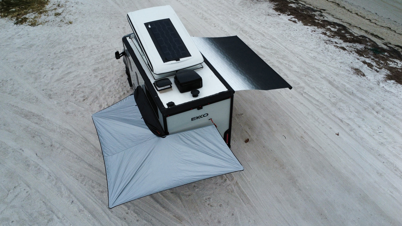 Overhead view of an EKKO off-road RV rental with deployed awnings on a sandy beach. Solar panel visible.
