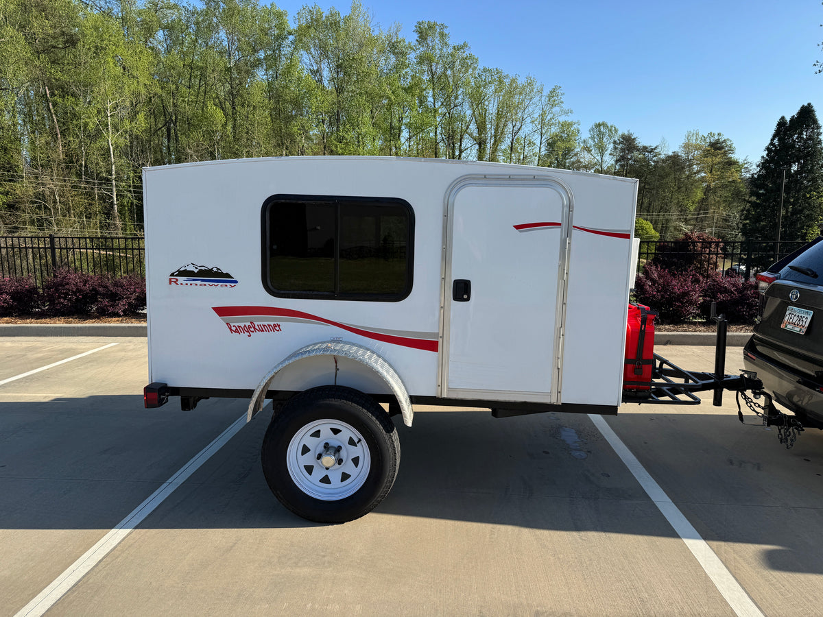 White Runaway RangeRunner travel trailer for RV rental, hitched to a black SUV in a parking lot.