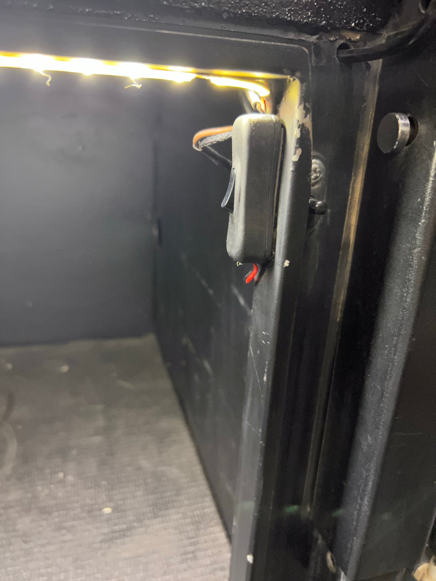 Bright LED strip lighting illuminates this RV rental storage compartment, featuring an accessible control switch on the wall.