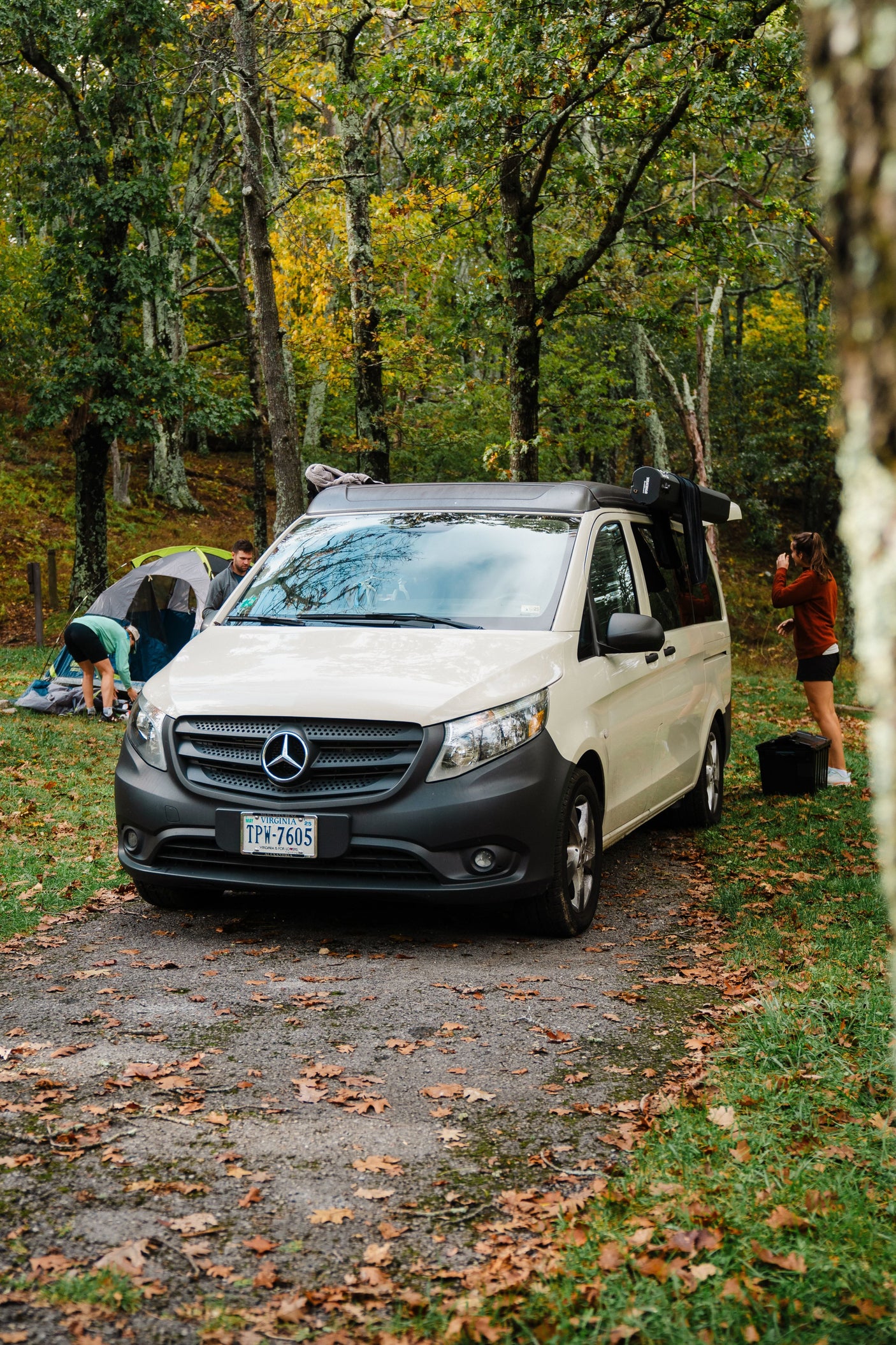 RV rental adventure: people set up camp with a white Mercedes van in an autumn forest.