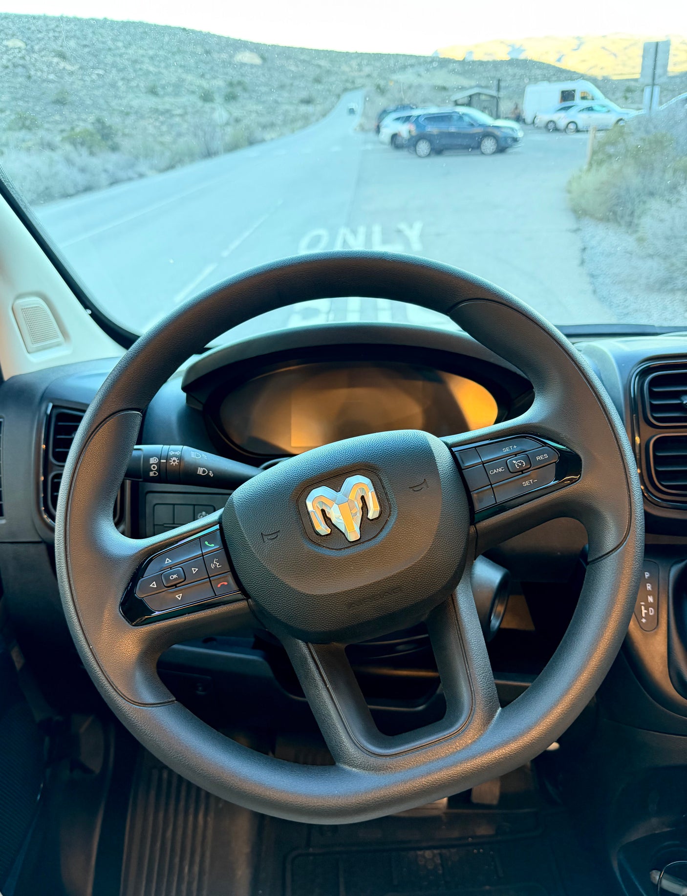 From an RV rental's driver seat, a Ram steering wheel and view of a road with parked cars and an RV ahead.