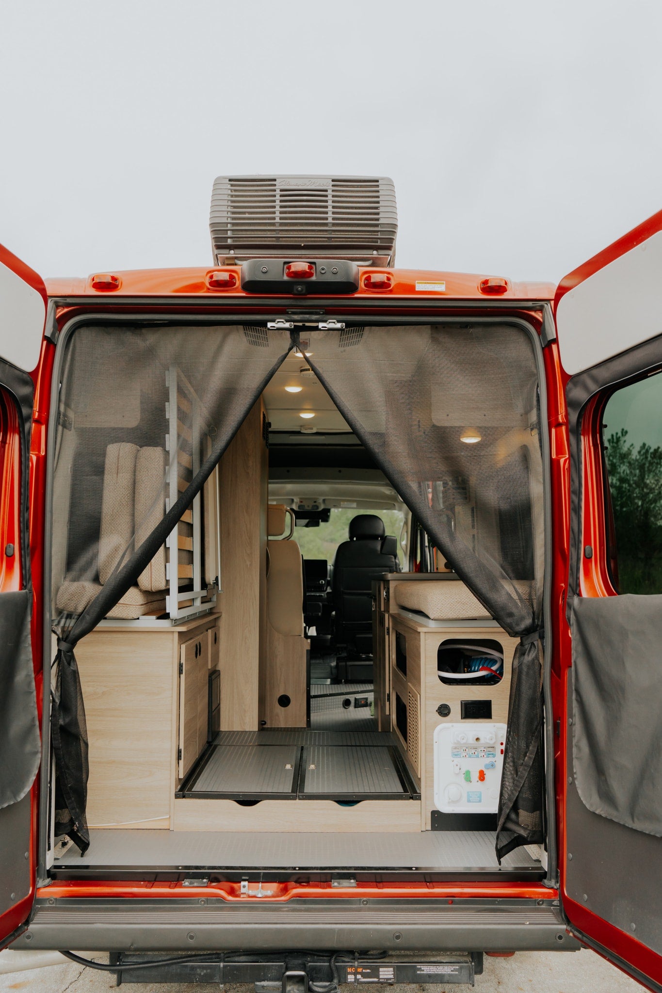 RV rental with open rear doors, revealing a cozy wood interior, mesh screen, and roof AC unit.