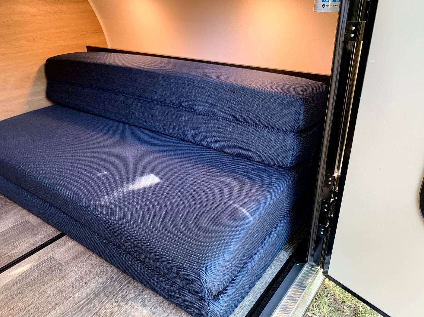 Inside an RV rental: a cozy navy blue folding bed or seating area. Features wood walls, floor, and open door.