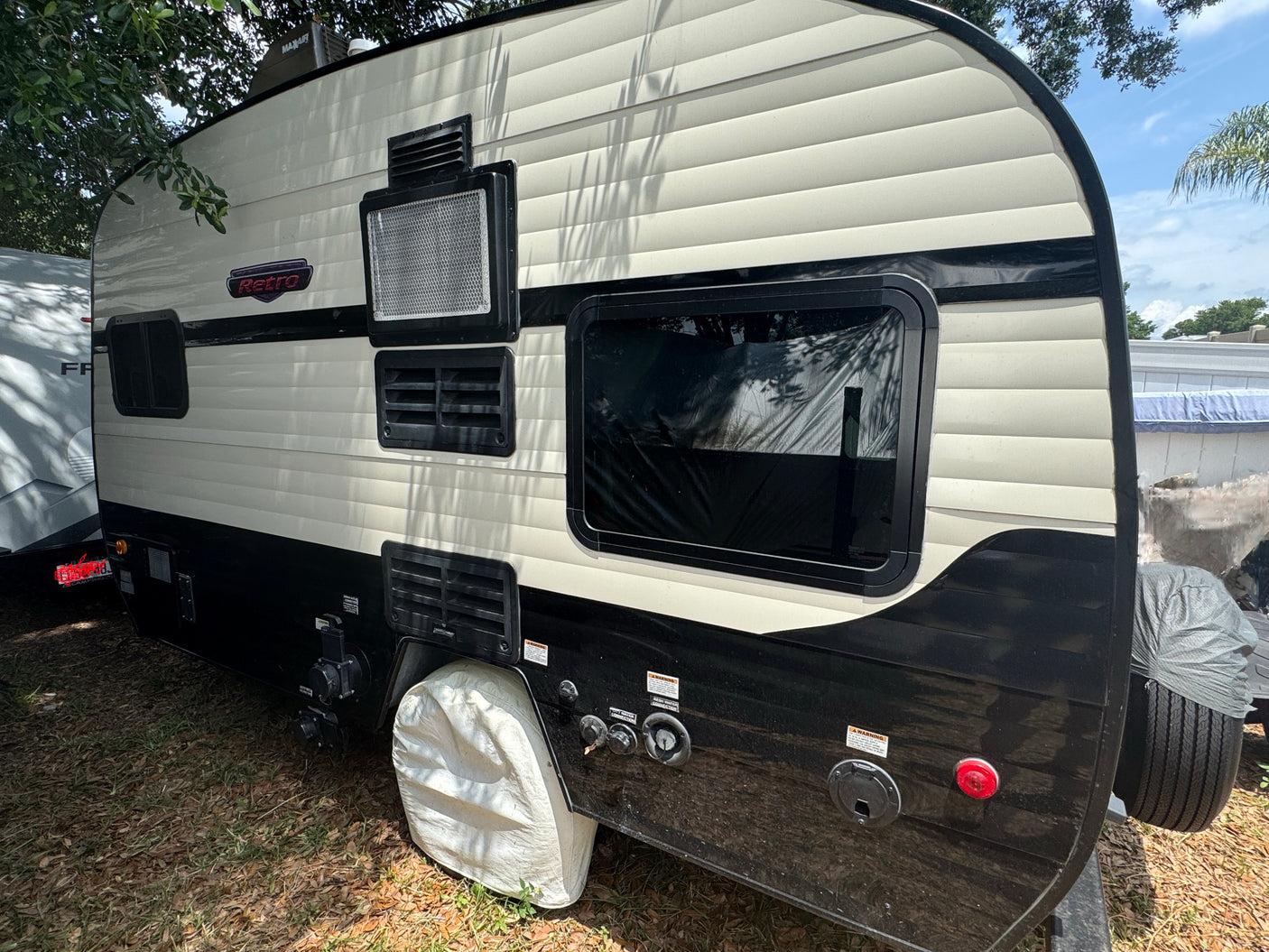 Side view of a "Retro" rv rental travel trailer, two-tone cream and black, showing utility hookups and vents.