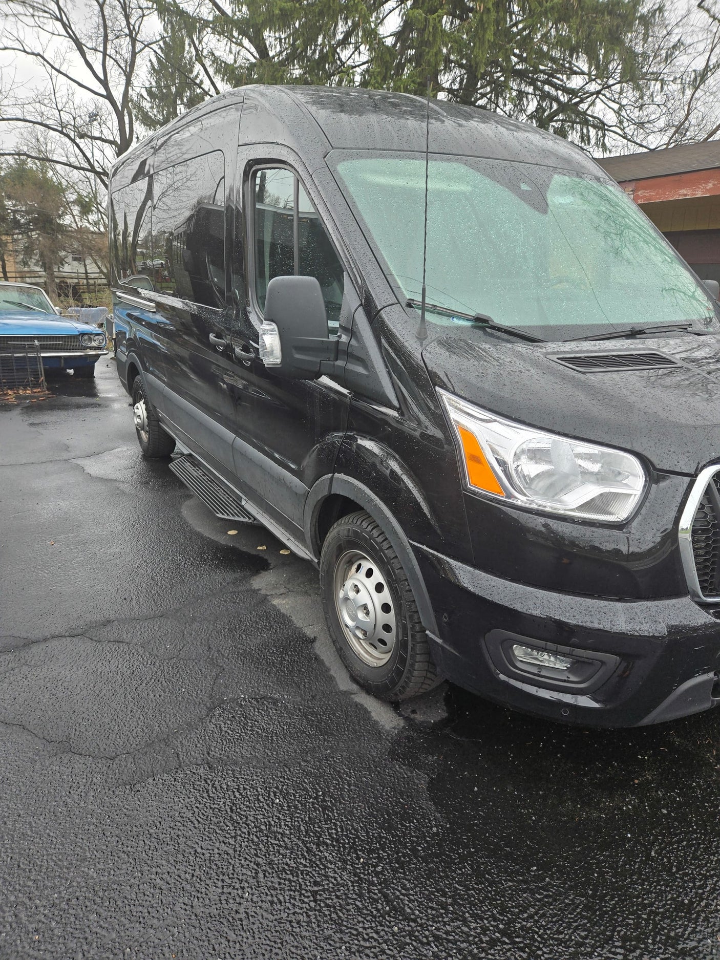 Black high-roof van, suitable for RV rental, parked on wet pavement with side steps and rain droplets.