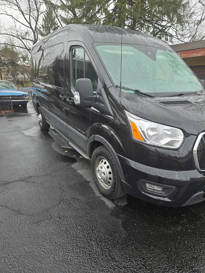 Black high-roof van, suitable for RV rental, parked on wet pavement with side steps and rain droplets.