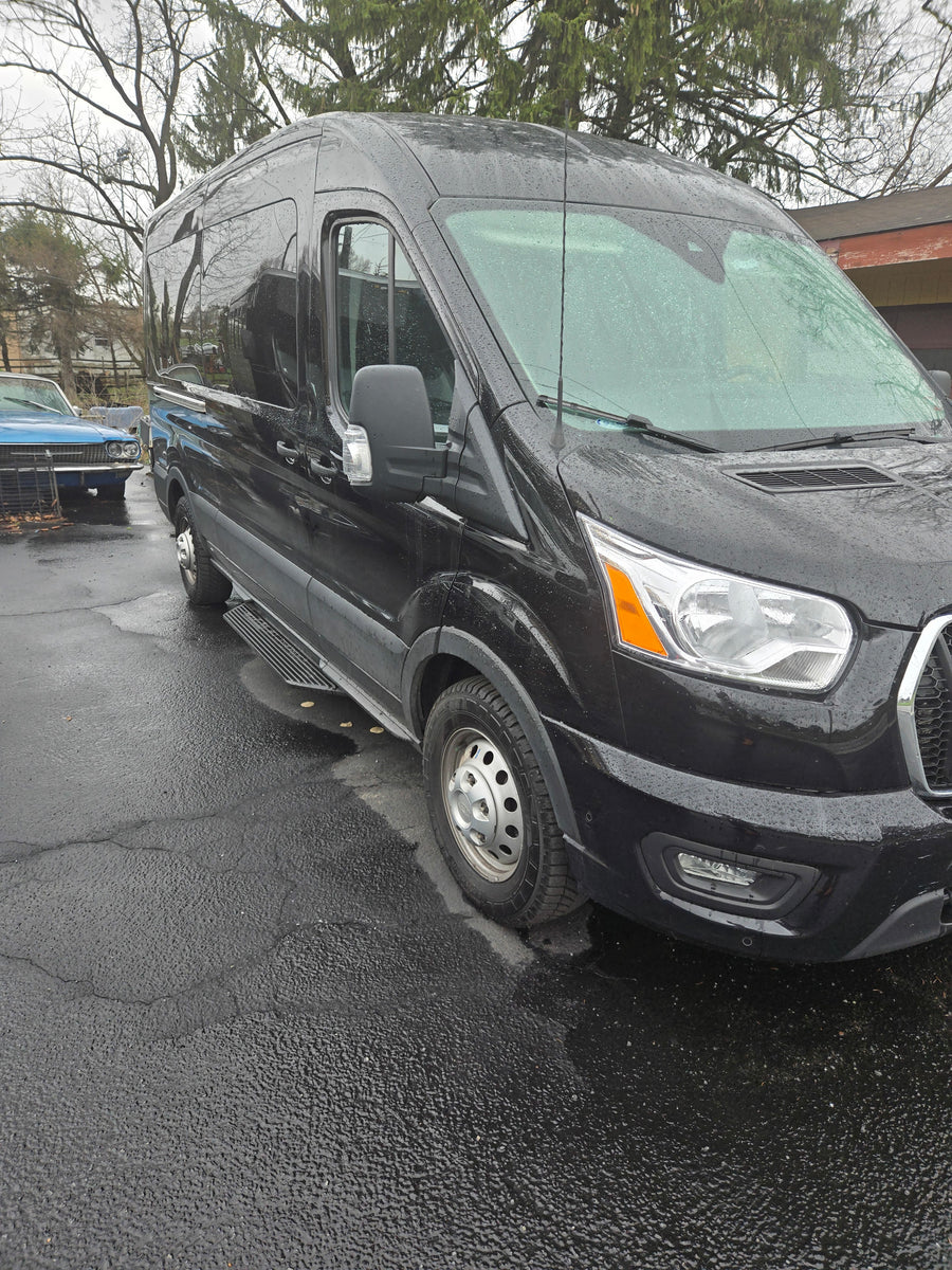 Black high-roof van, suitable for RV rental, parked on wet pavement with side steps and rain droplets.