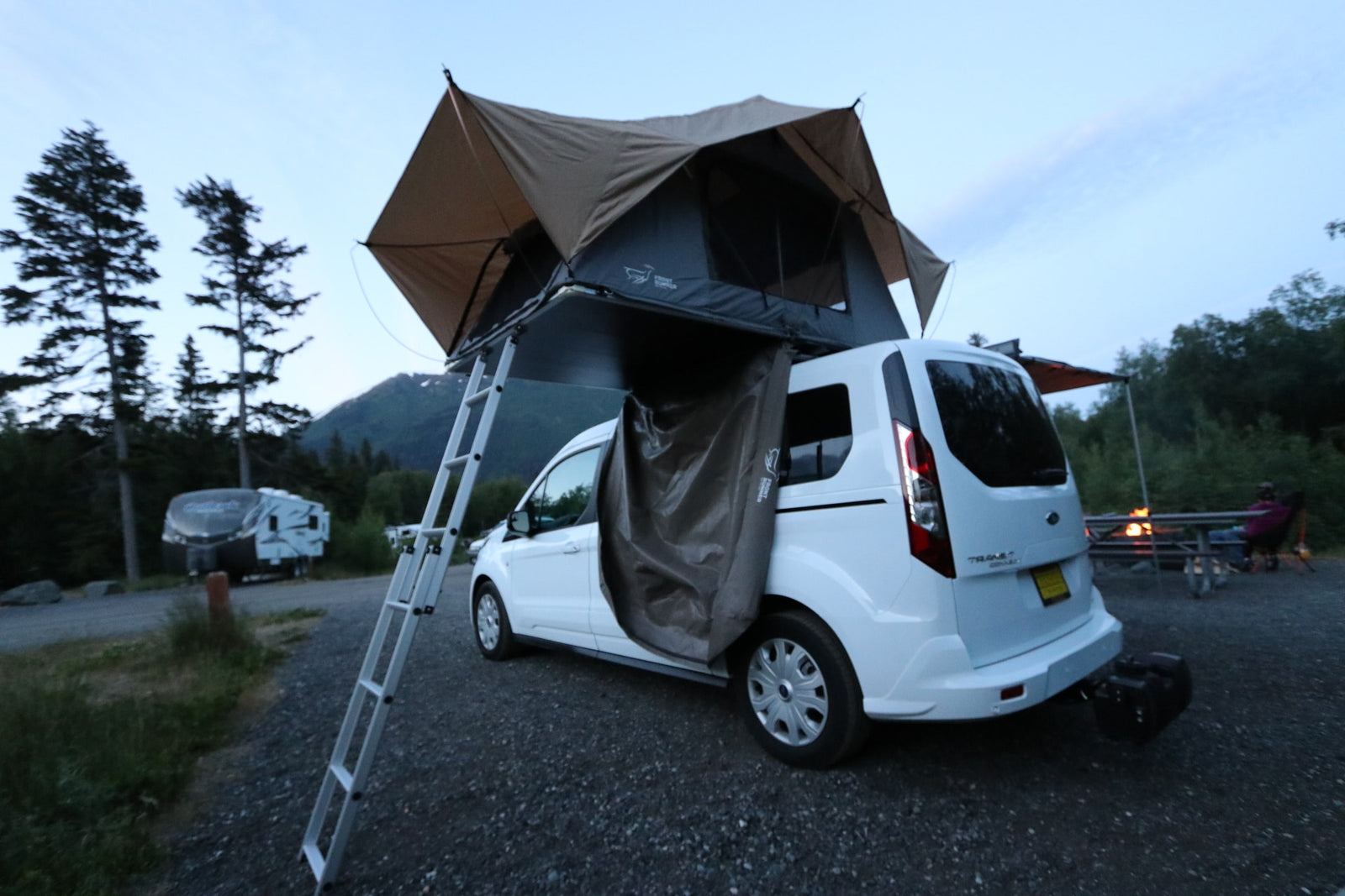Camping adventure with an RV rental van featuring a rooftop tent and annex, set up at a scenic campground.
