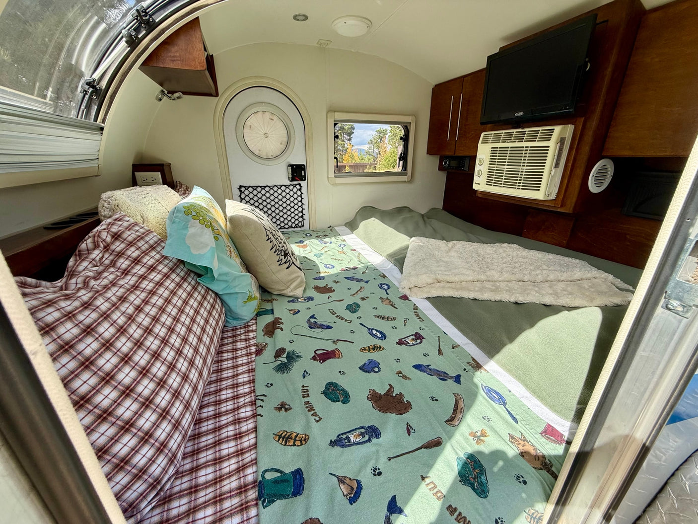 Cozy rv rental interior: comfy bed with nature-themed bedding, AC, TV, ready for your next adventure.