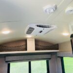 RV rental interior featuring a central AC unit, bright LED lights, and netted overhead storage above a window. — photo 13