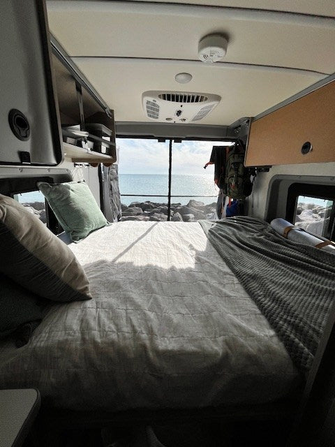 perfect for washing off by the beautiful coastal waters. Palm trees line the view.|Discover coastal views with an RV rental! This silver camper van sits by calm blue water under a bright
