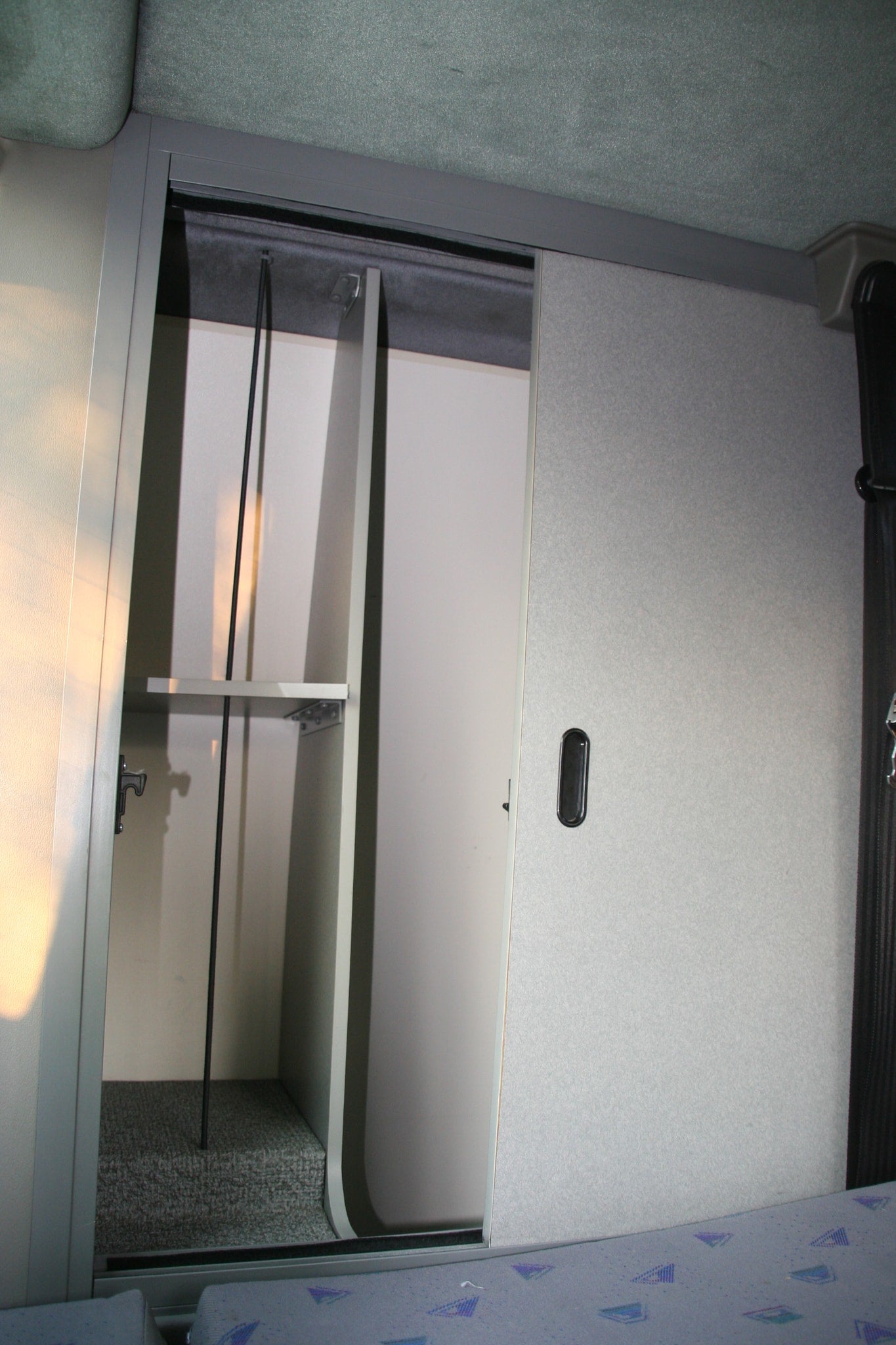 Open overhead storage compartment in an RV rental, revealing shelves and a handle. Convenient interior organization.