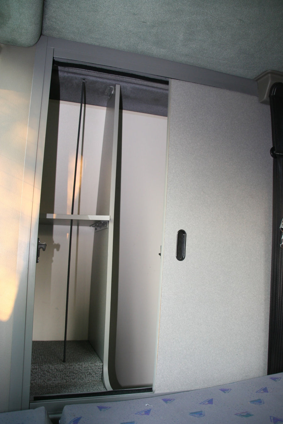 Open overhead storage compartment in an RV rental, revealing shelves and a handle. Convenient interior organization.