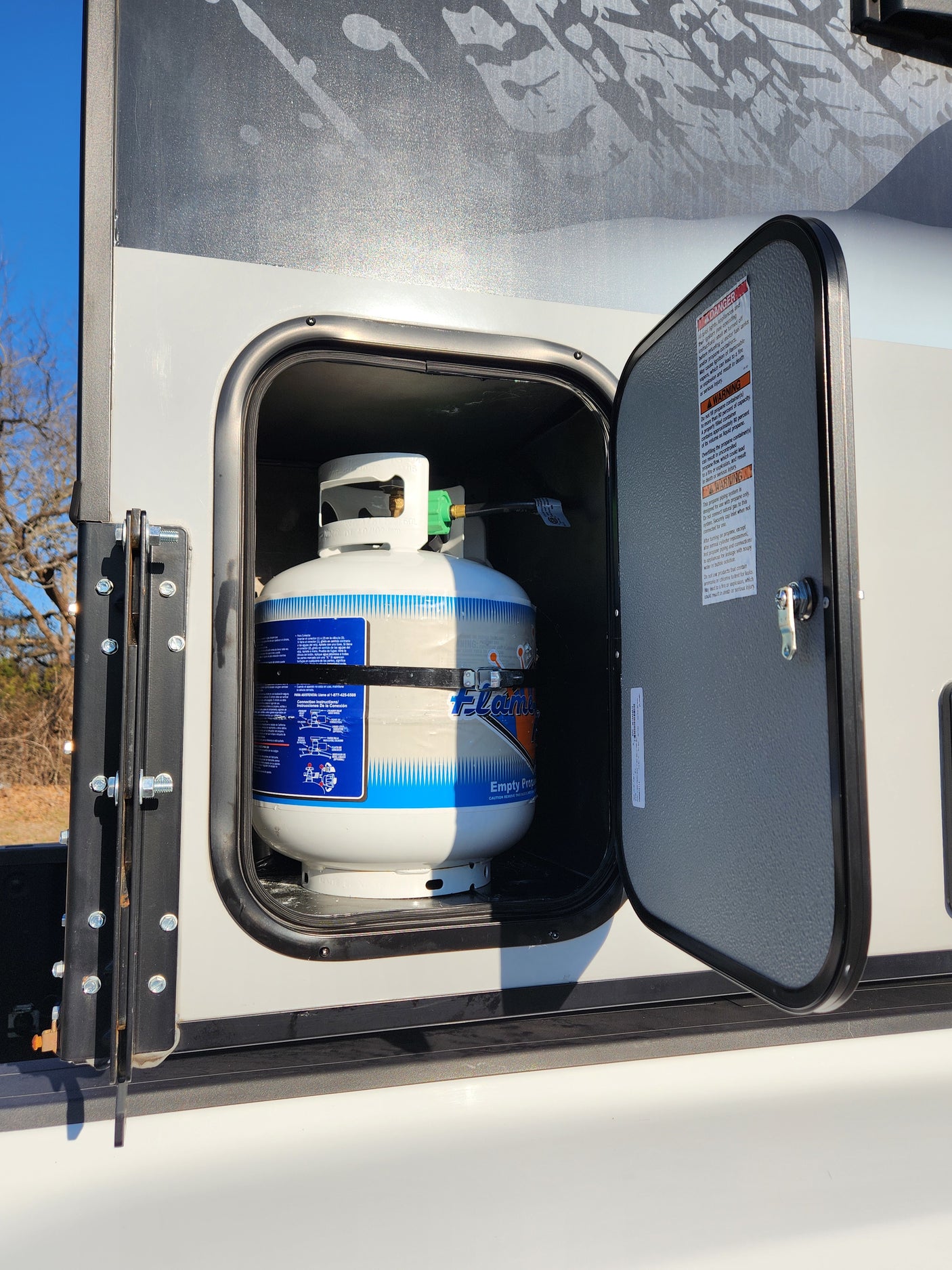 RV rental: Open compartment showing propane tank and safety warnings inside.