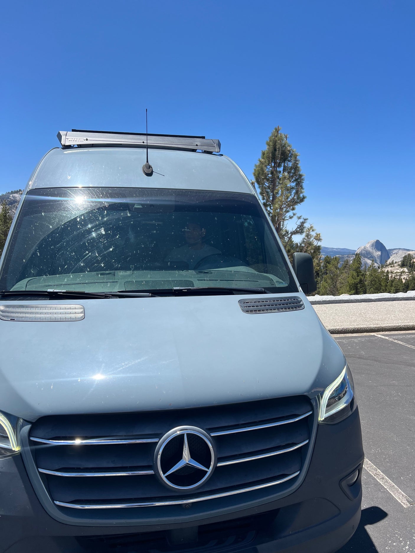A grey Mercedes-Benz Sprinter RV rental parked, featuring a Westin roof rack, with Yosemite's iconic Half Dome in the background.