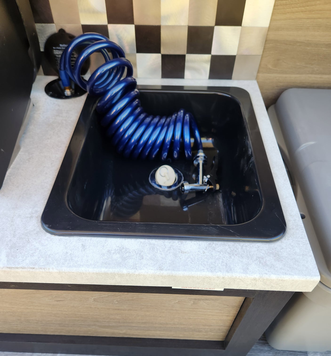 Compact RV rental utility sink with blue coiled shower hose & faucet, perfect for a camper's outdoor washing station.