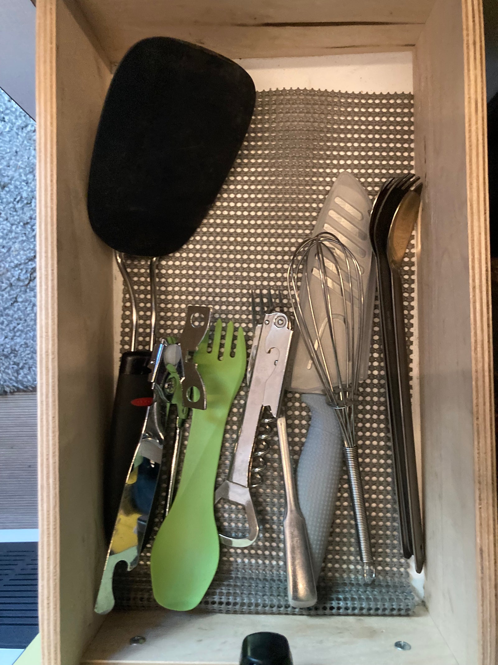 Essential kitchen tools for your RV rental: spatula, whisk, can opener, corkscrew, and cutlery neatly arranged in a lined drawer.