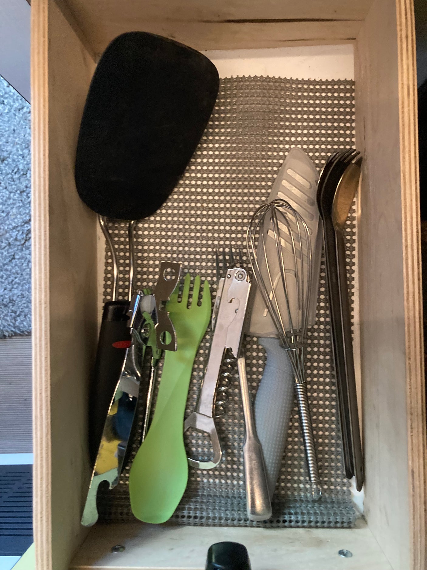 Essential kitchen tools for your RV rental: spatula, whisk, can opener, corkscrew, and cutlery neatly arranged in a lined drawer.
