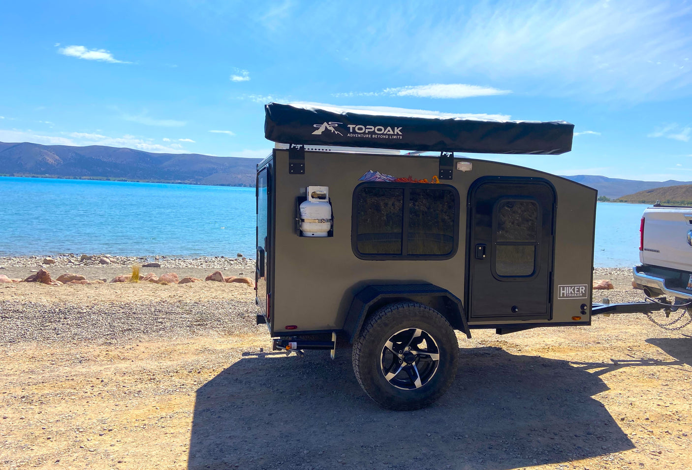 An off-grid Hiker Trailer RV rental parked lakeside, ideal for scenic outdoor camping adventures.