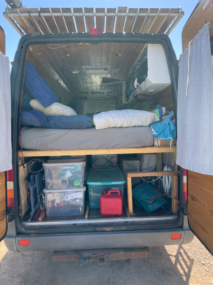 Rear view of an RV rental's custom camper van interior, featuring a bed, organized storage, and a roof rack.
