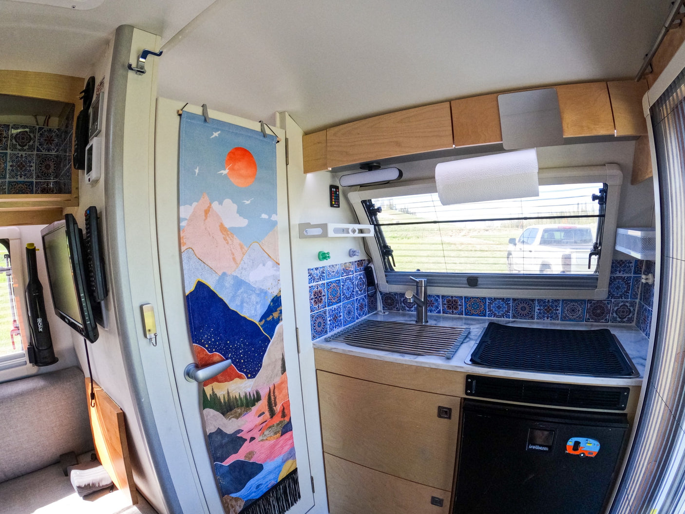 RV rental interior: A compact kitchen with a sink, tiled backsplash, wooden cabinets, and a fridge below.