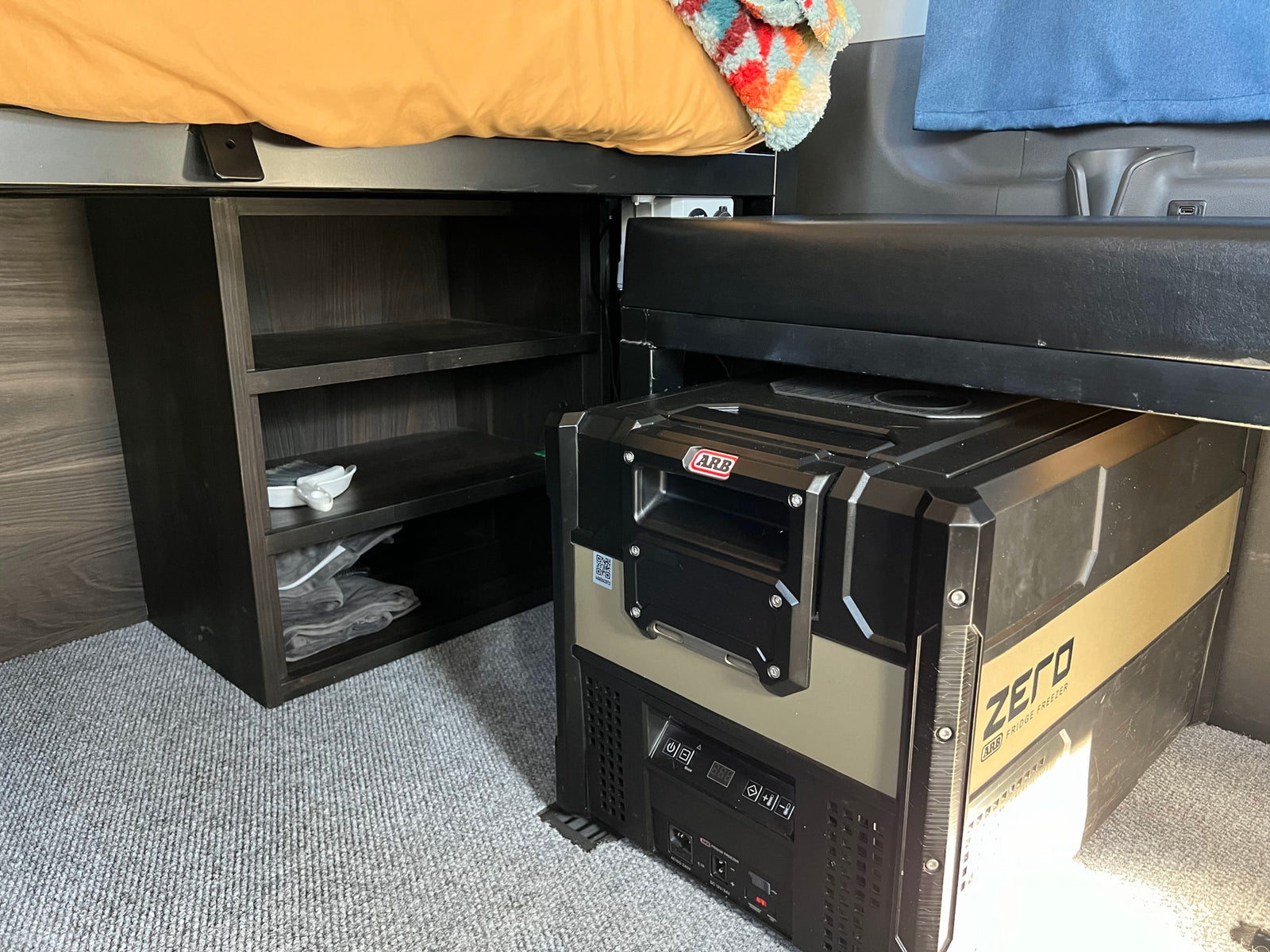 RV rental interior: smart setup includes a raised bed, dark storage shelves, and an ARB ZERO portable fridge/freezer.