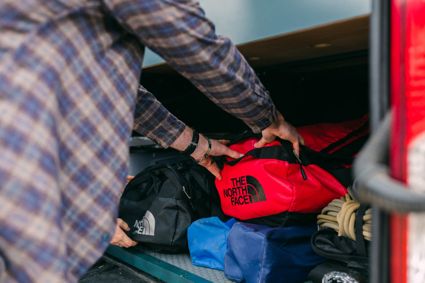 Packing up for adventure in your RV rental! A person in a plaid shirt neatly organizes North Face duffel bags and gear. — photo 17