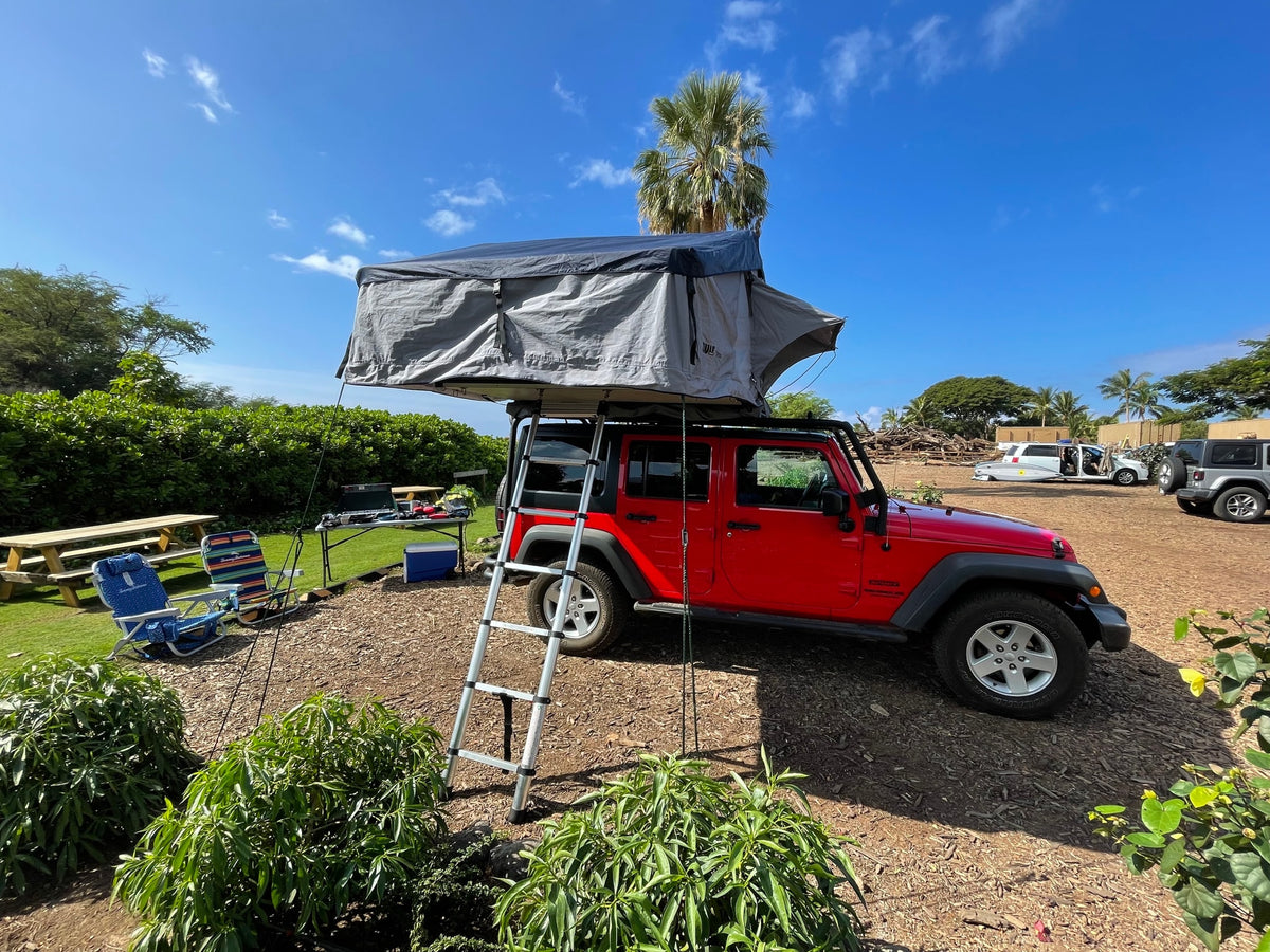 Red Jeep Wrangler with grey rooftop tent, ladder extended, set up at a sunny outdoor camp. Perfect for an RV rental trip. — photo 20