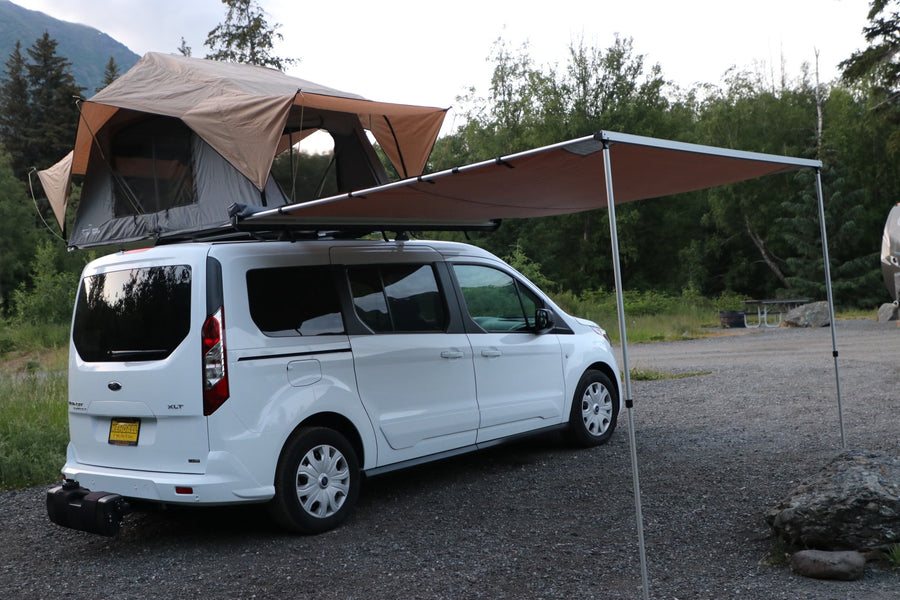 White Ford Transit Connect **rv rental**, set up with a rooftop tent and side awning, ready for outdoor camping adventures.