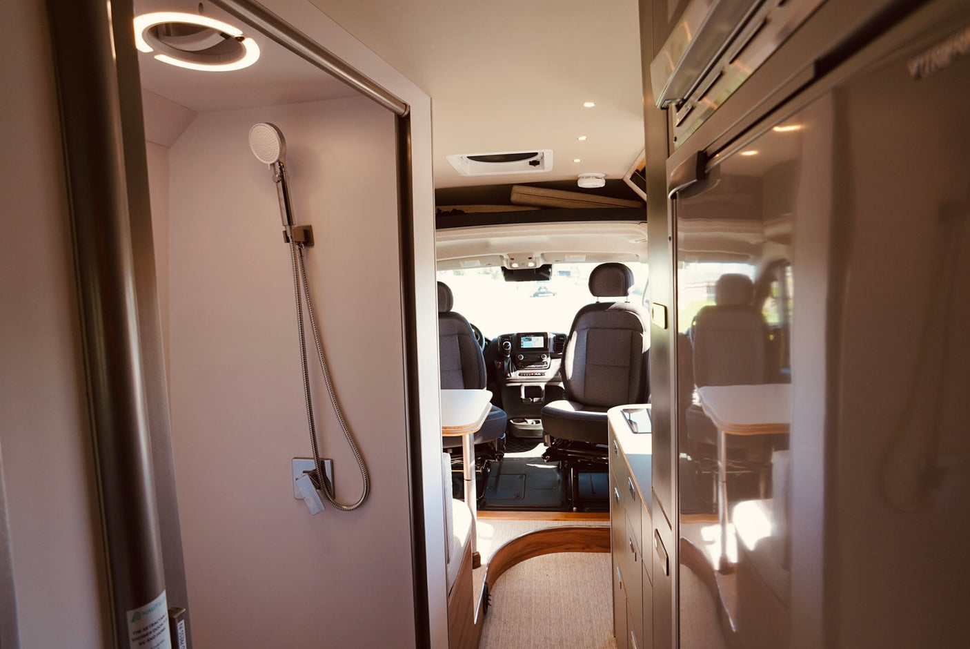 Inside a spacious RV rental: A well-lit shower on the left, fridge on the right, leading to the driver's cabin.