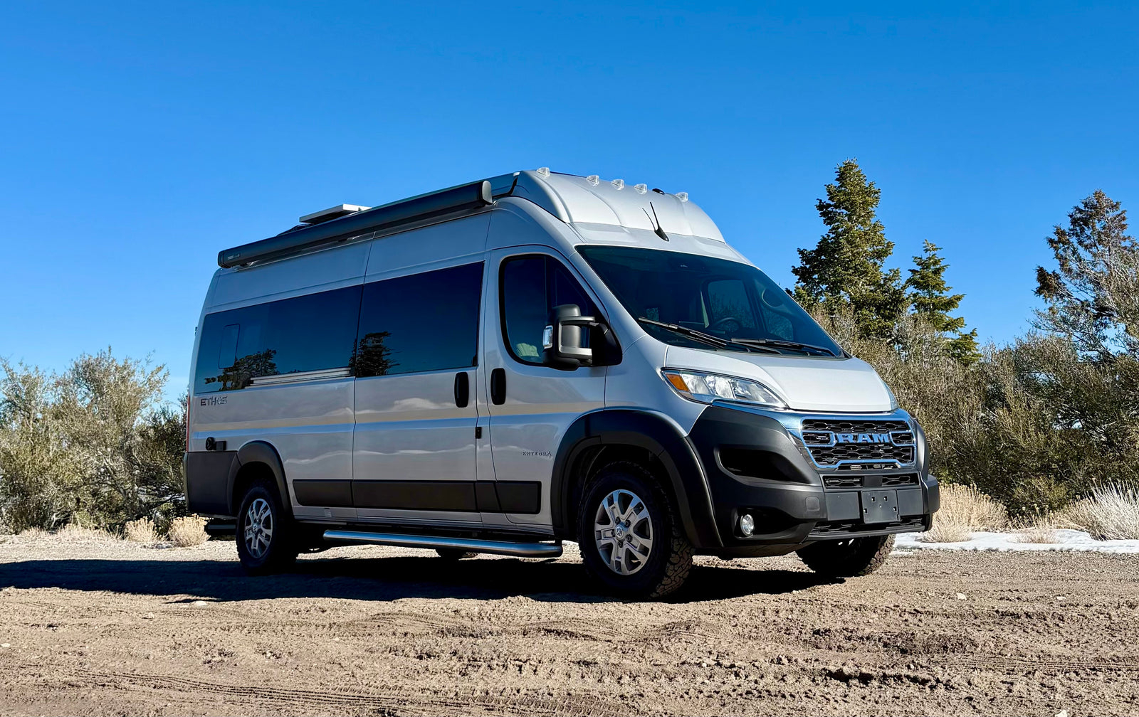 Silver Integra Ethos Class B camper van, a perfect rv rental for adventure, parked on a dirt path under a clear blue sky.